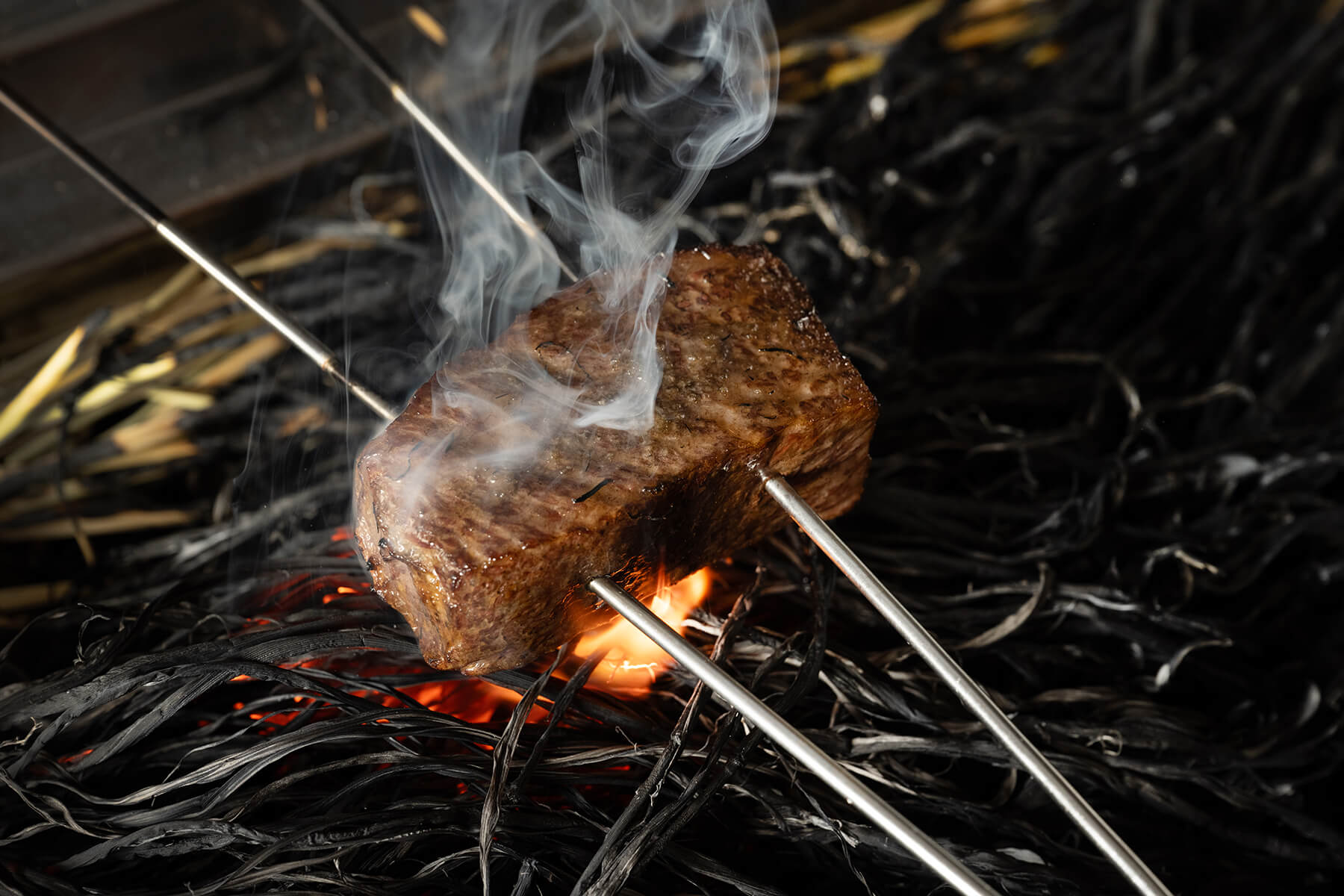 Rice-straw-infused Wagyu being seared over burning straw