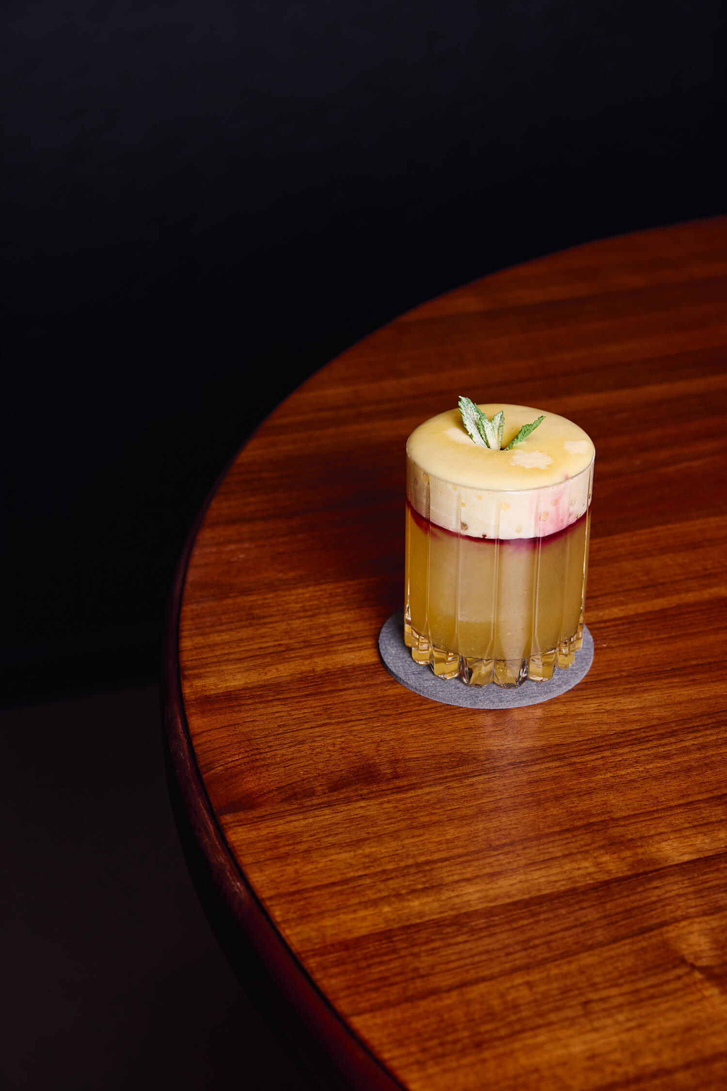 Yellow cocktail with a foamy top and herb garnish